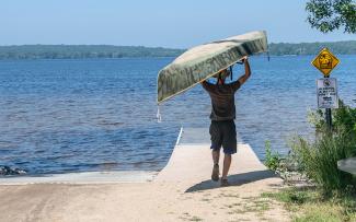 A person carrying a canoe over their head towards the boat ramp at Burlingame State Park Picnic Area in Charlestown