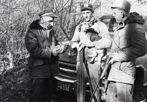 black & white image of officer checking the license of two hunters with a dog