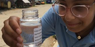 Person holding small labelled jar with a water sample in it.