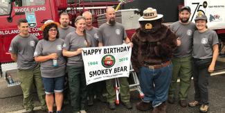 Group of people next to fire truck holding a Happy Birthday Smokey Bear sign