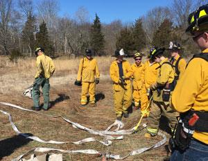 several people in yellow fire gear standing with hoses in a field