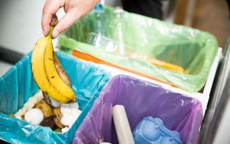 A hand places a banana peel into a kitchen composting bin