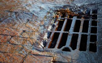 Water flowing down through a manhole cover on a sunny spring day