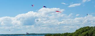 Kites flying in a blue sky with puffy white clouds at Brenton Point State Park in Newport