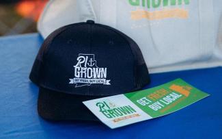 A dark colored ball cap and bumper sticker with the RI Grown logo