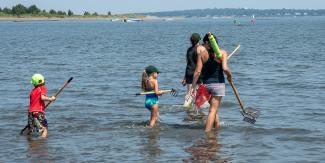 A family carrying bull rakes in the shallow waters at Rocky Point State Park