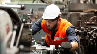 A person with a white hard hat and yellow safety vest leaning operating manufacturing machinery