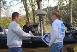 A volunteer provides outreach material to a boater at a freshwater boat ramp that gives tips for preventing the spread of invasive aquatic plants