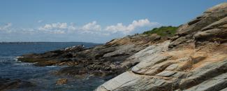 Rocky cliffs meet the ocean against a blue sky at Beavertail State Park in Jamestown