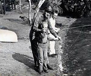 A historic photo of an environmental police officer standing behind a young angler and assisting in casting out a fishing pole
