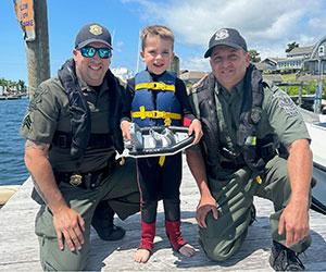 Two environmental police officers smiling with a small child wearing a life jacket