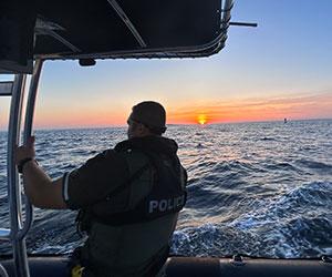 Silhouette of a law enforcement officer looking out at a sunset from a police boat