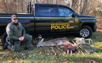 RI Environmental Police Officer kneels beside a poached deer and seized hunting equipment
