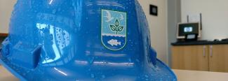 Blue hard hat with water droplets on it and the DEM logo sitting on a desk with a computer in the background