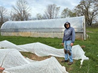 Farmer from West Bay Community Action stands in agricultural field with greenhouse behind him